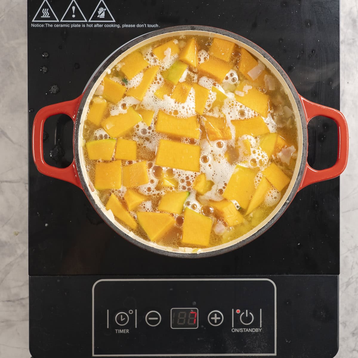 Stock simmering on stove top with ingredients for baked pumpkin risotto inside.