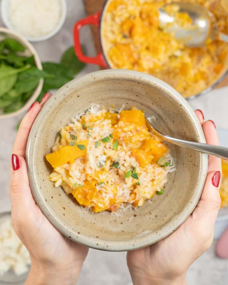 Womans hands holding a bowl of baked pumpkin risotto with fork inside.