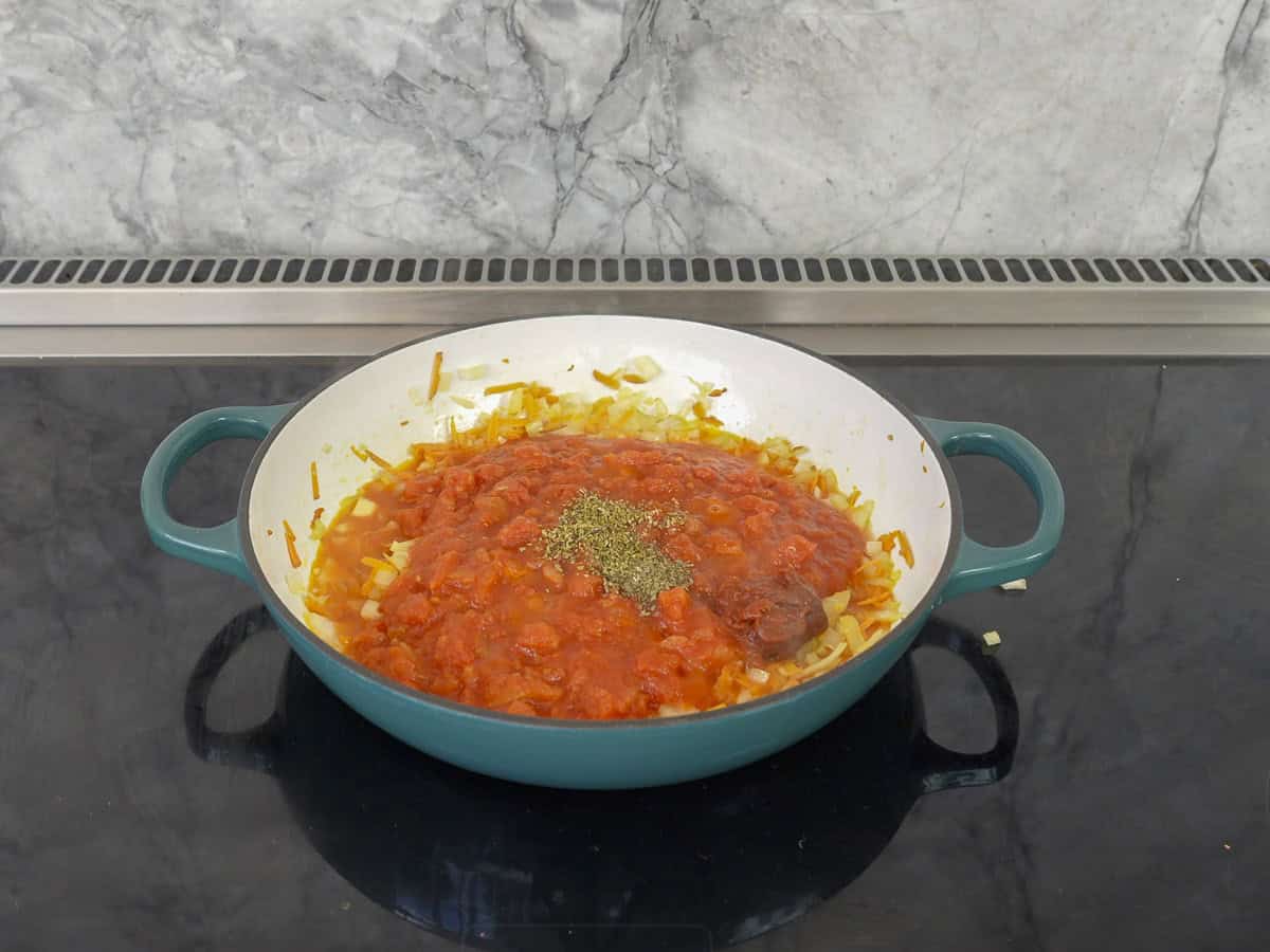 A pan with tomato sauce and herbs on top of a stove.