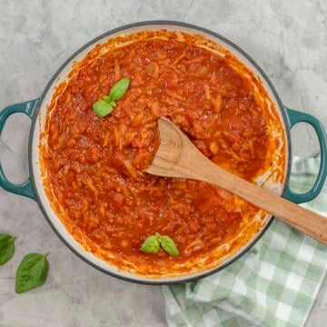 A pan of marinara sauce garnished with basil leaves.