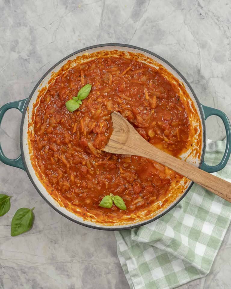 A pan of marinara sauce garnished with basil leaves.