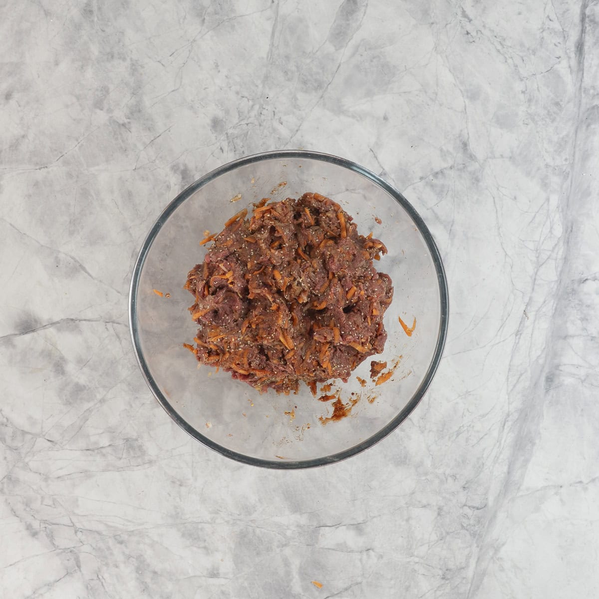 Ingredients for meatloaf combined together in a large glass bowl on benchtop.