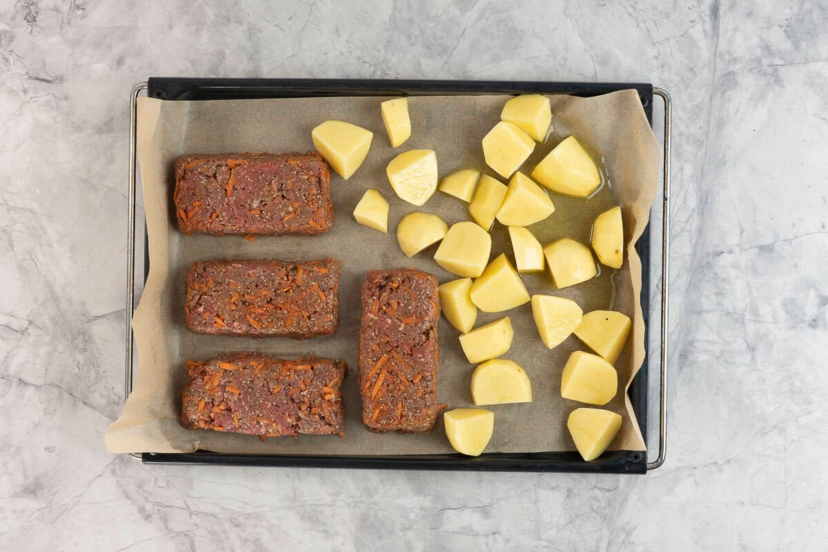 Four mini rectangle meatloaf's on a lined baking tray with chopped potatoes.
