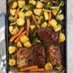 Lined baking tray with roasted vegetables and four mini rectangle meatloaf's, with cheese melted on top.