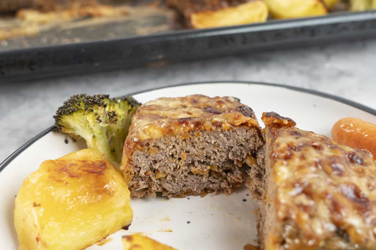 Dinner plate with roast vegetables and and meatloaf cut in half showing the inside.