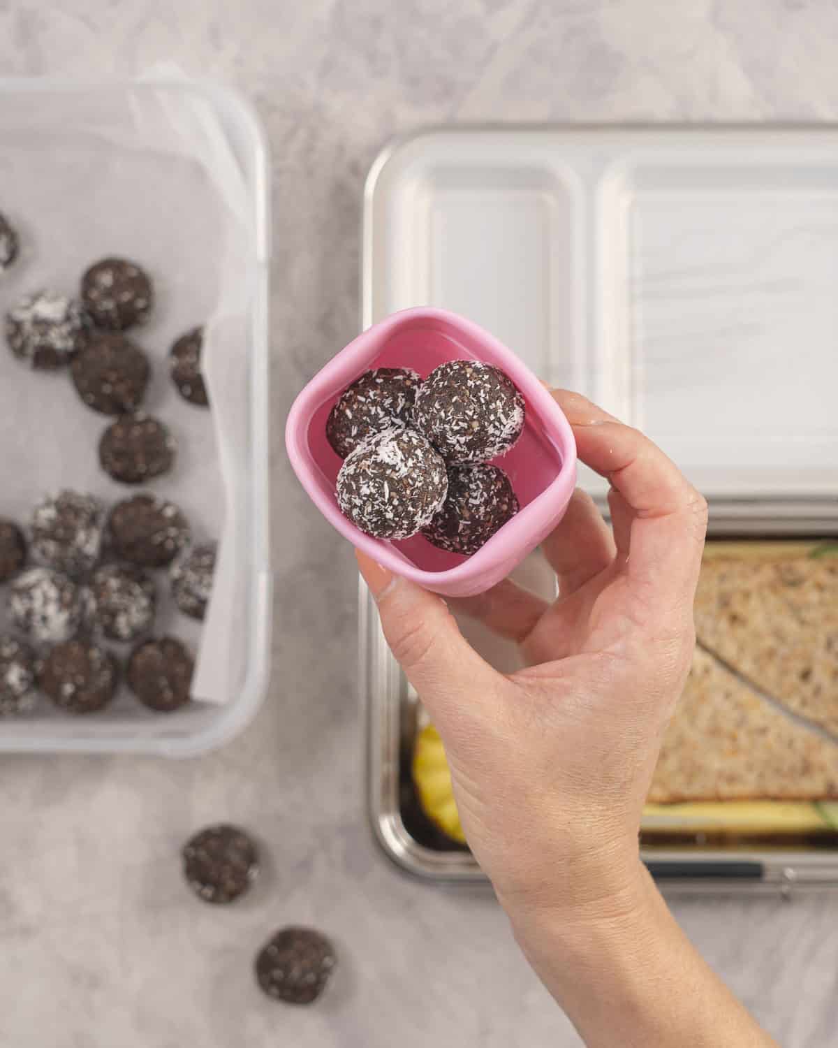 Hand holding a small silicone container with four weetbix balls inside.