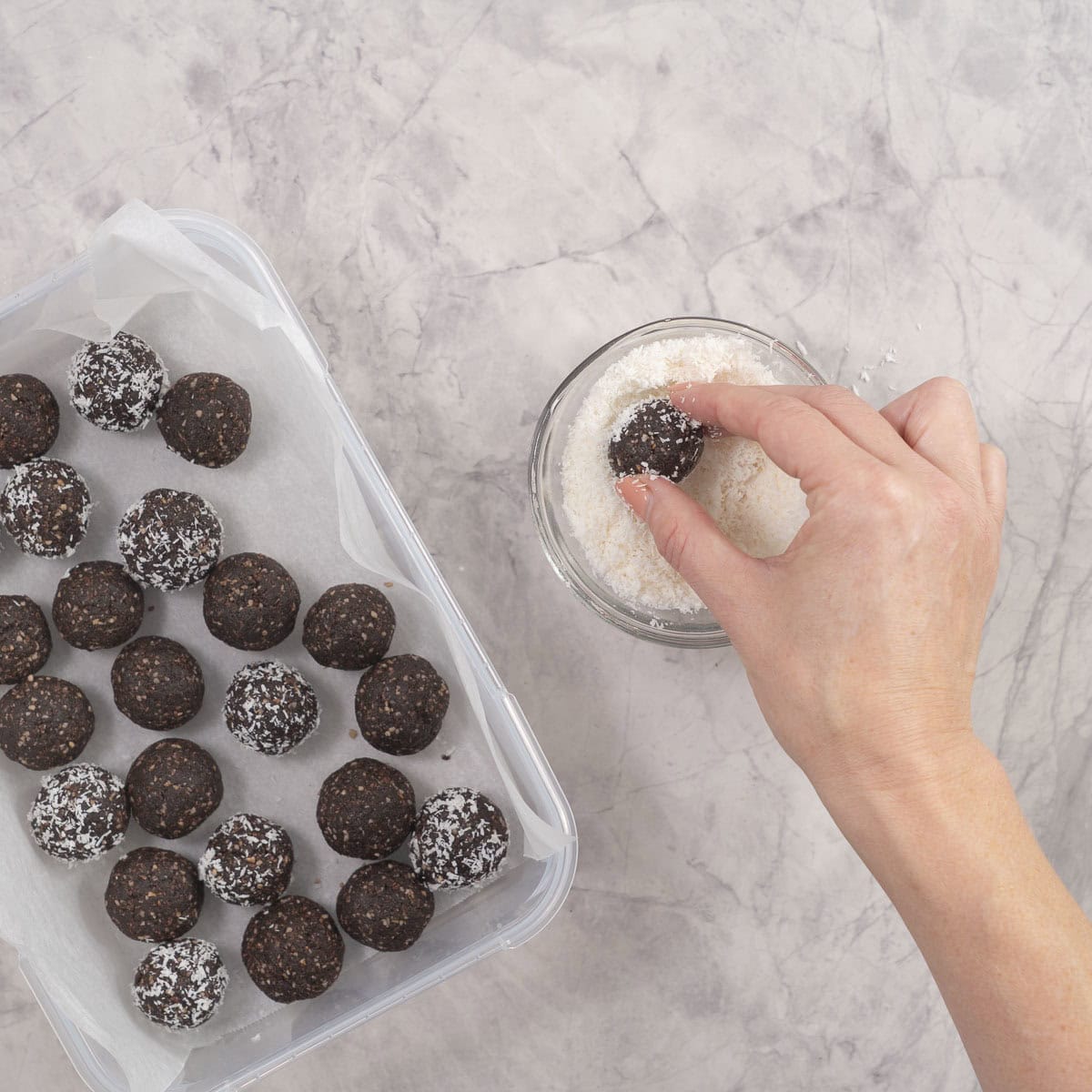 Hand holding a weetbix bliss ball rolling it in small glass bowl of shredded coconut.