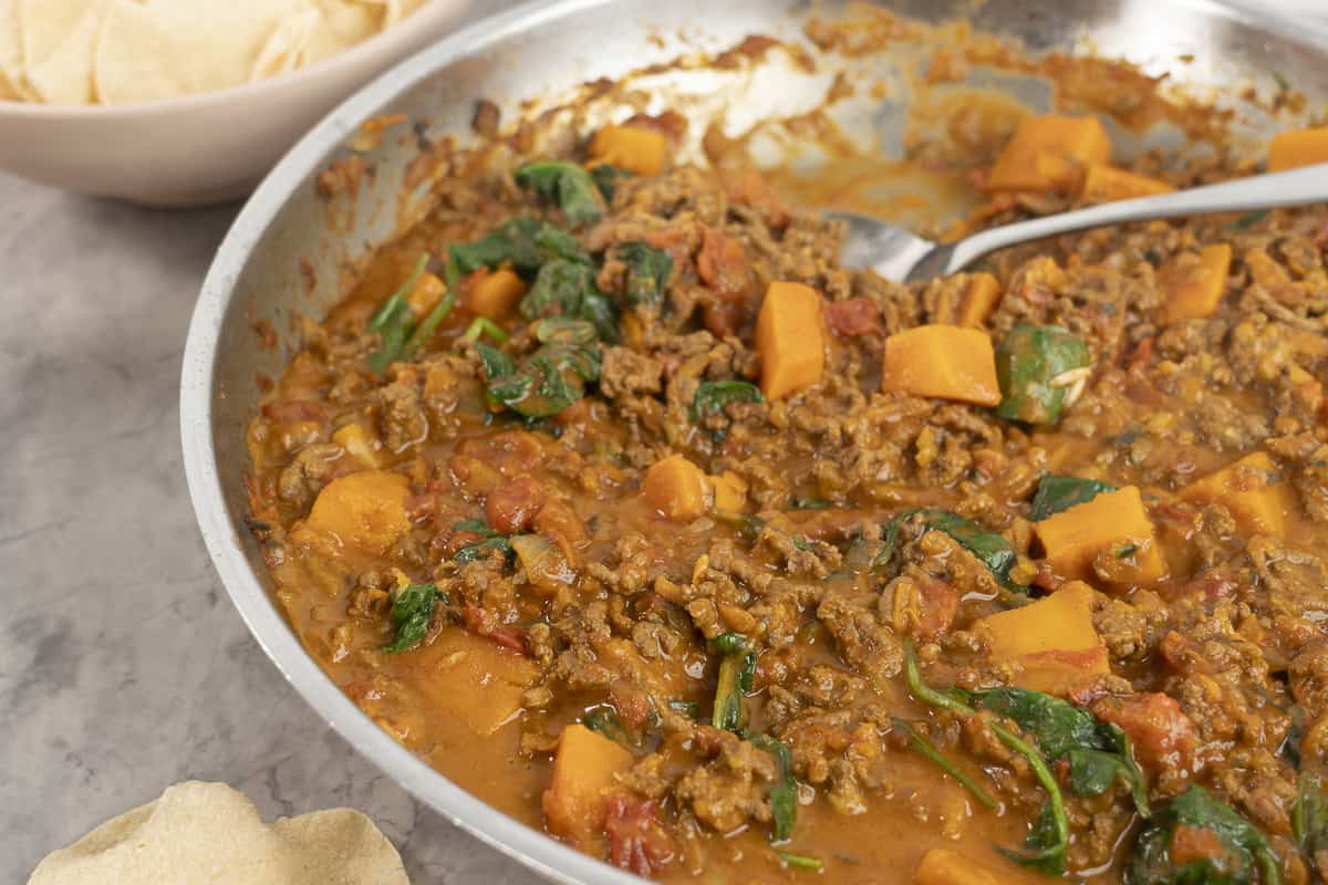 Pan of mince curry on benchtop with serving spoon inside.