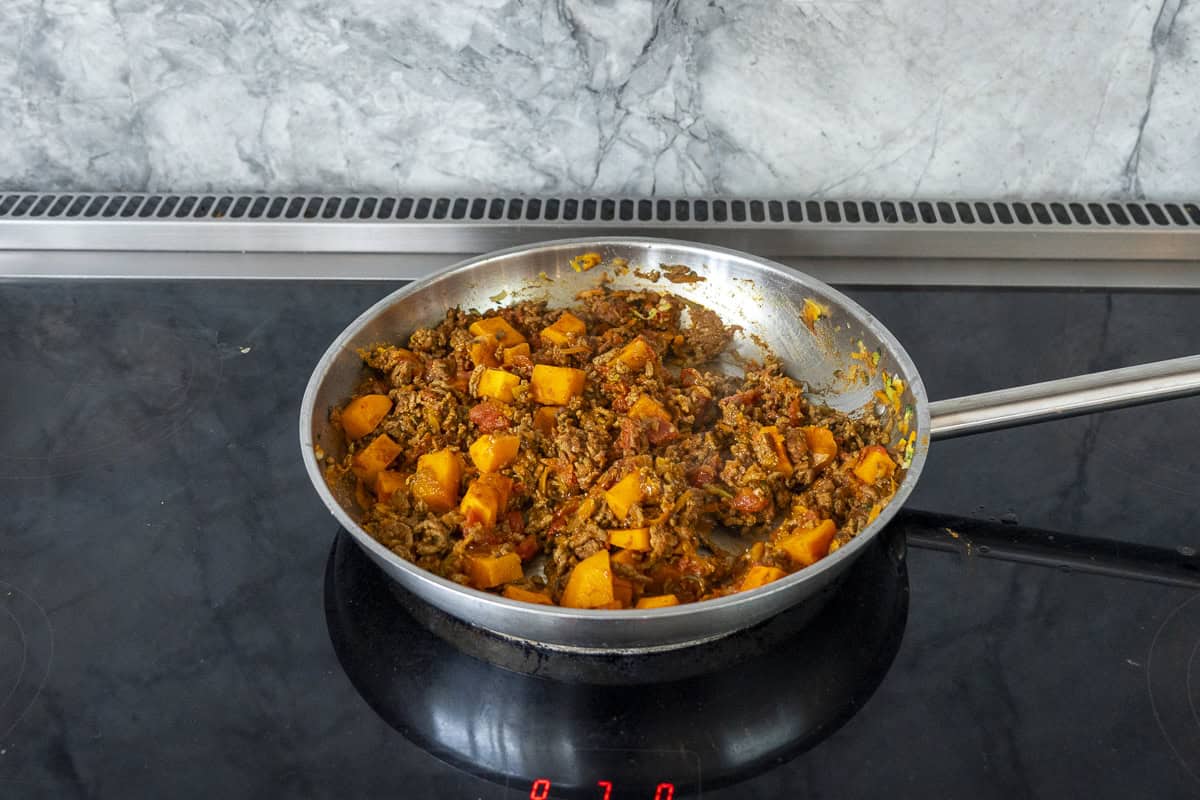 Pan of mince curry on stove top with pumpkin added.