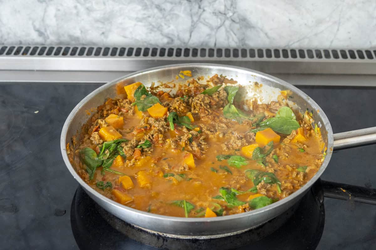 Pan of mince curry on stove top with pumpkin and spinach added.