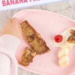 a baby picking up a strip of banana French toast from a pink baby plate of toast, yogurt and raspberries. With text overlay; banana French toast, healthy first foods.