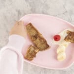 Baby hand reaching for a piece of French toast from a pink baby plate.