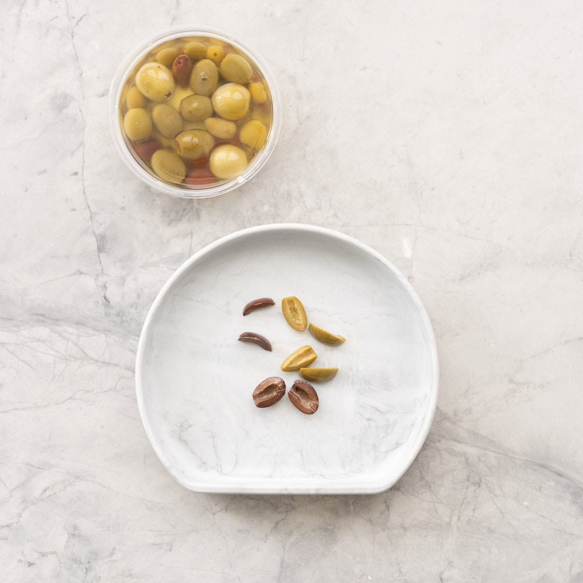 A bowl of olives next to a baby plate with sliced olives.