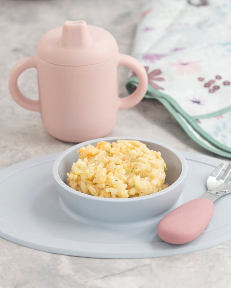 Blue silicone baby bowl with cheesy rice inside, toddler fork with pink silicone handle, pink silicone babu cup on benchtop.