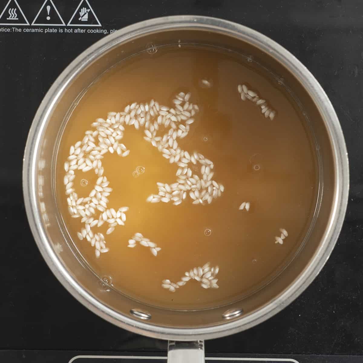 Rice and stock in a pot cooking on an electric element.