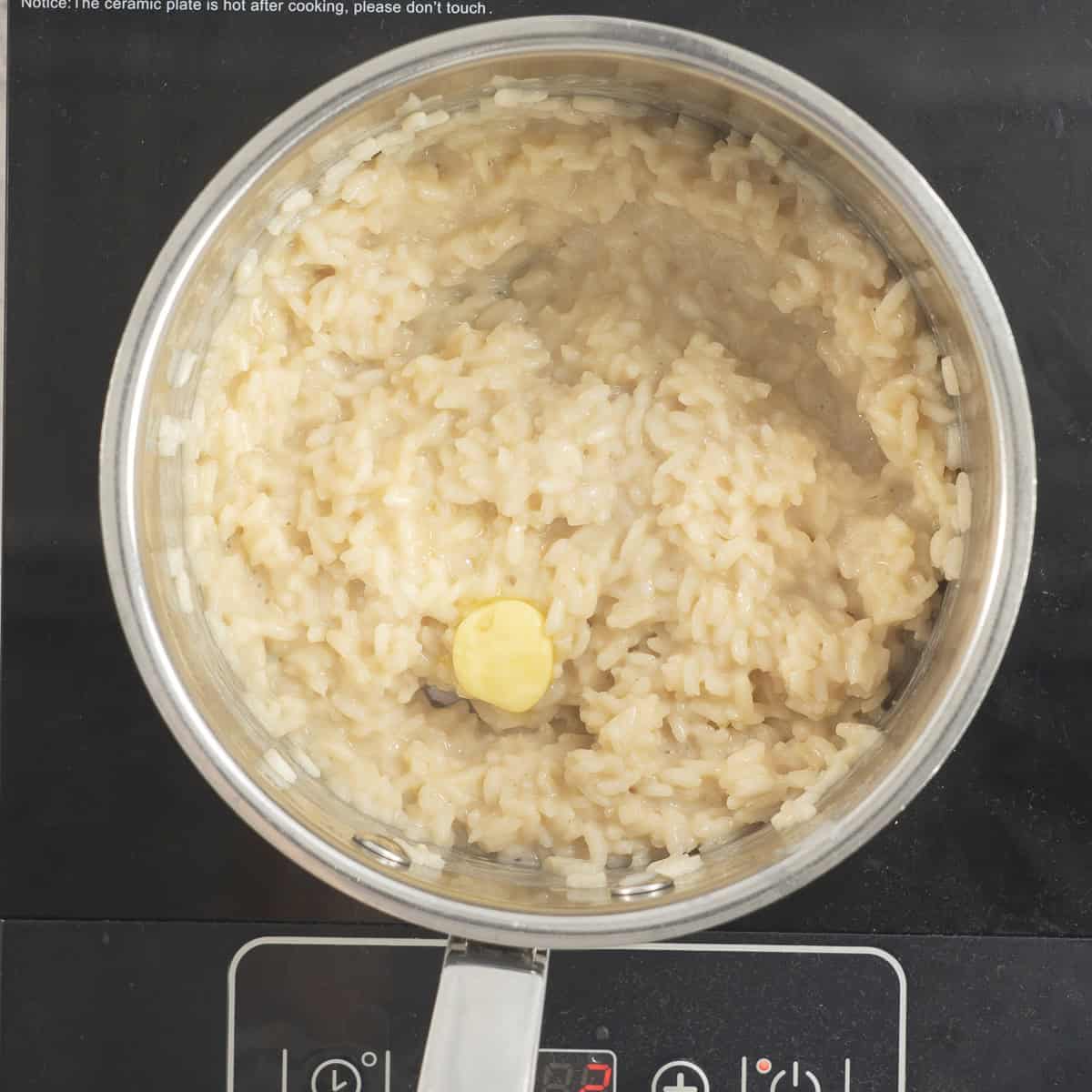 Softened rice with dollop of butter inside a pot on an electric element.