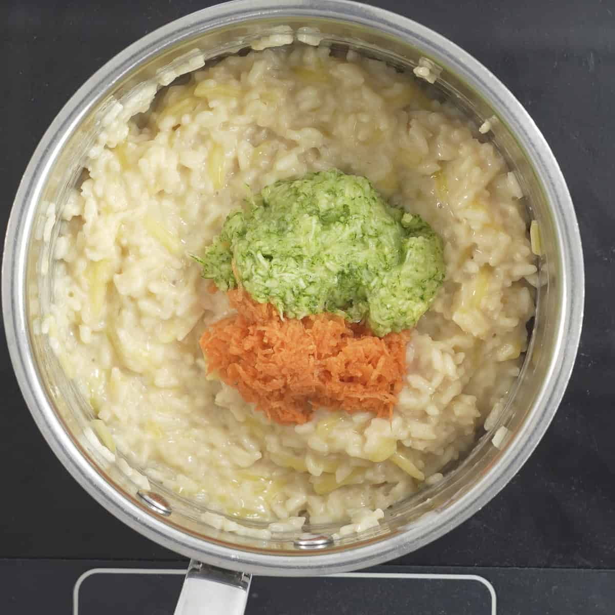 Creamy rice with very finely grated carrot and zucchini. sitting on top ready to be stirred through.