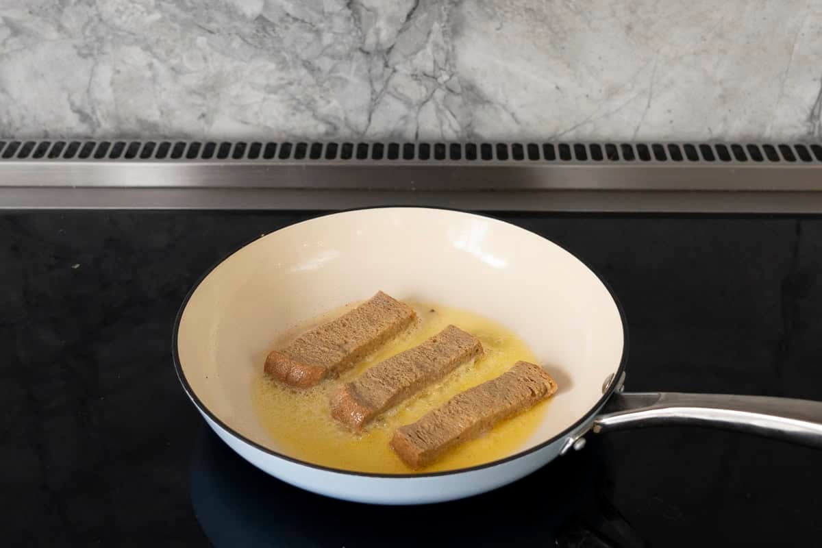 Three slice of bread in a pan on stovetop frying in egg mixture and butter.