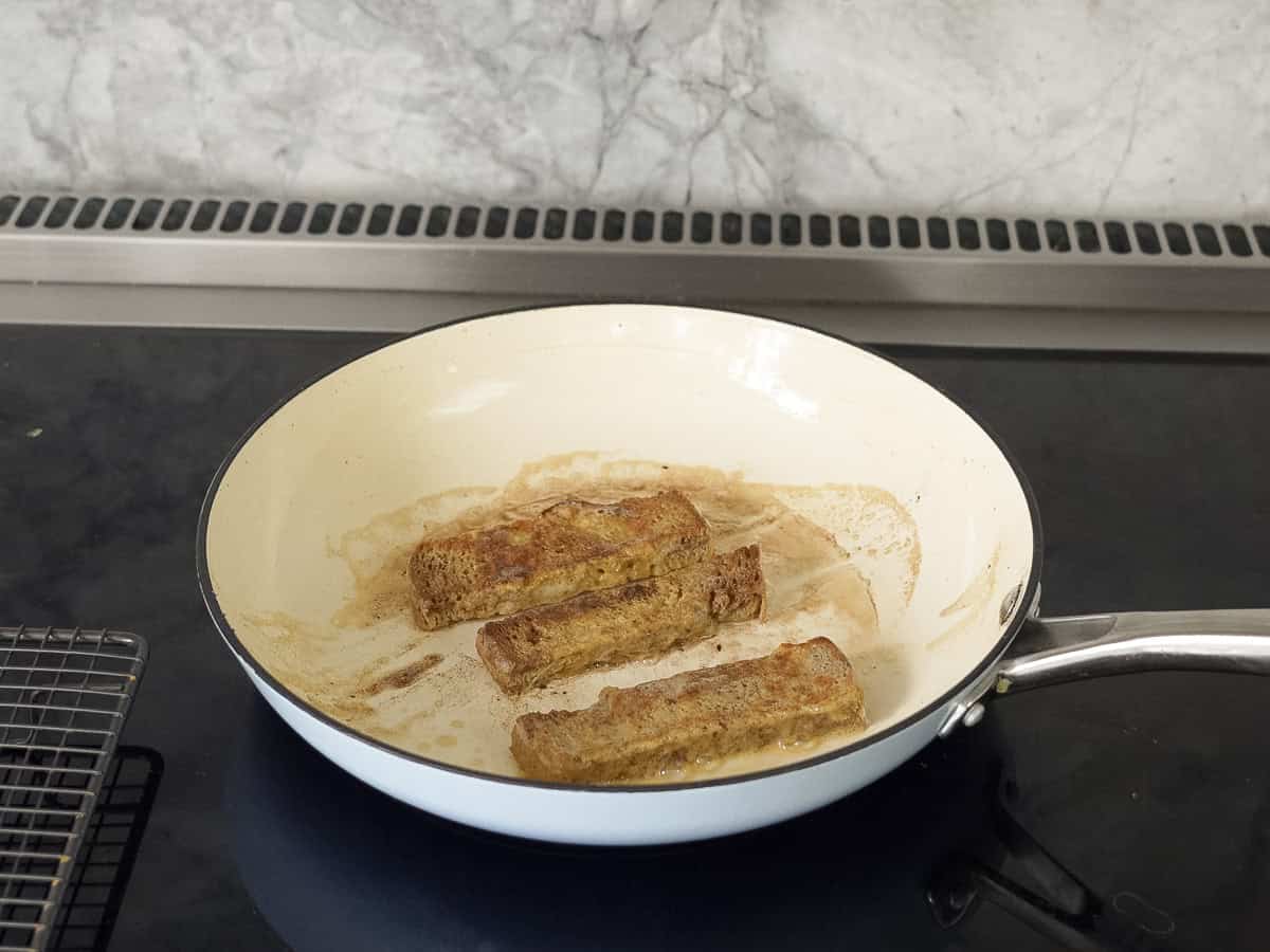 Three pieces of sliced bread cooking in a pan on stove top.