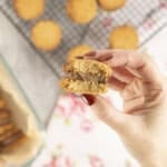 Womans hand holding a cookie with chocolate peanut butter mixture inside and two cookies on the outside with a bite taken out of it.