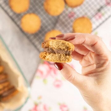 Womans hand holding a cookie with chocolate peanut butter mixture inside and two cookies on the outside with a bite taken out of it.