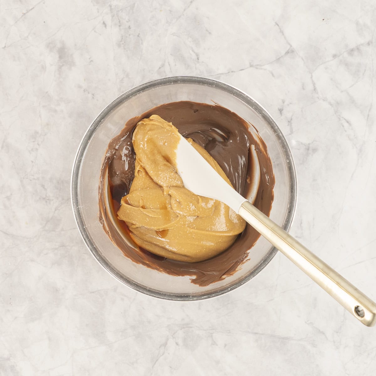Peanut butter added into bowl of melted chocolate with spatula inside.