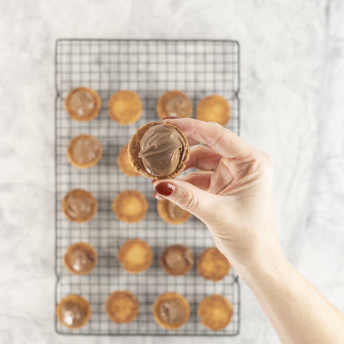 Womans hand holding a cookie with dollop of peanut butter/chocolate mixture on top.