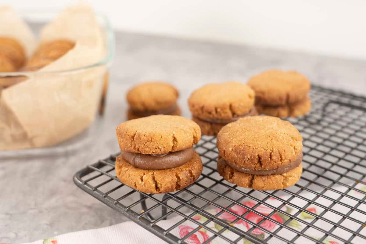 Five peanut butter sandwich cookies on a cooling rack with layer of chocolate peanut butter mixture inside.