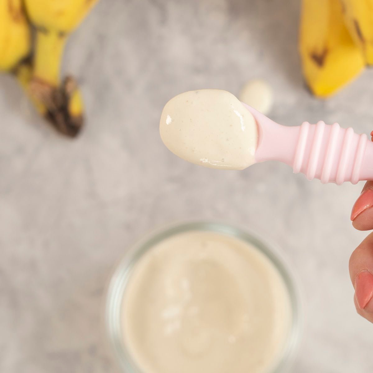 Small glass container with pink baby spoon scooping out banana pudding.