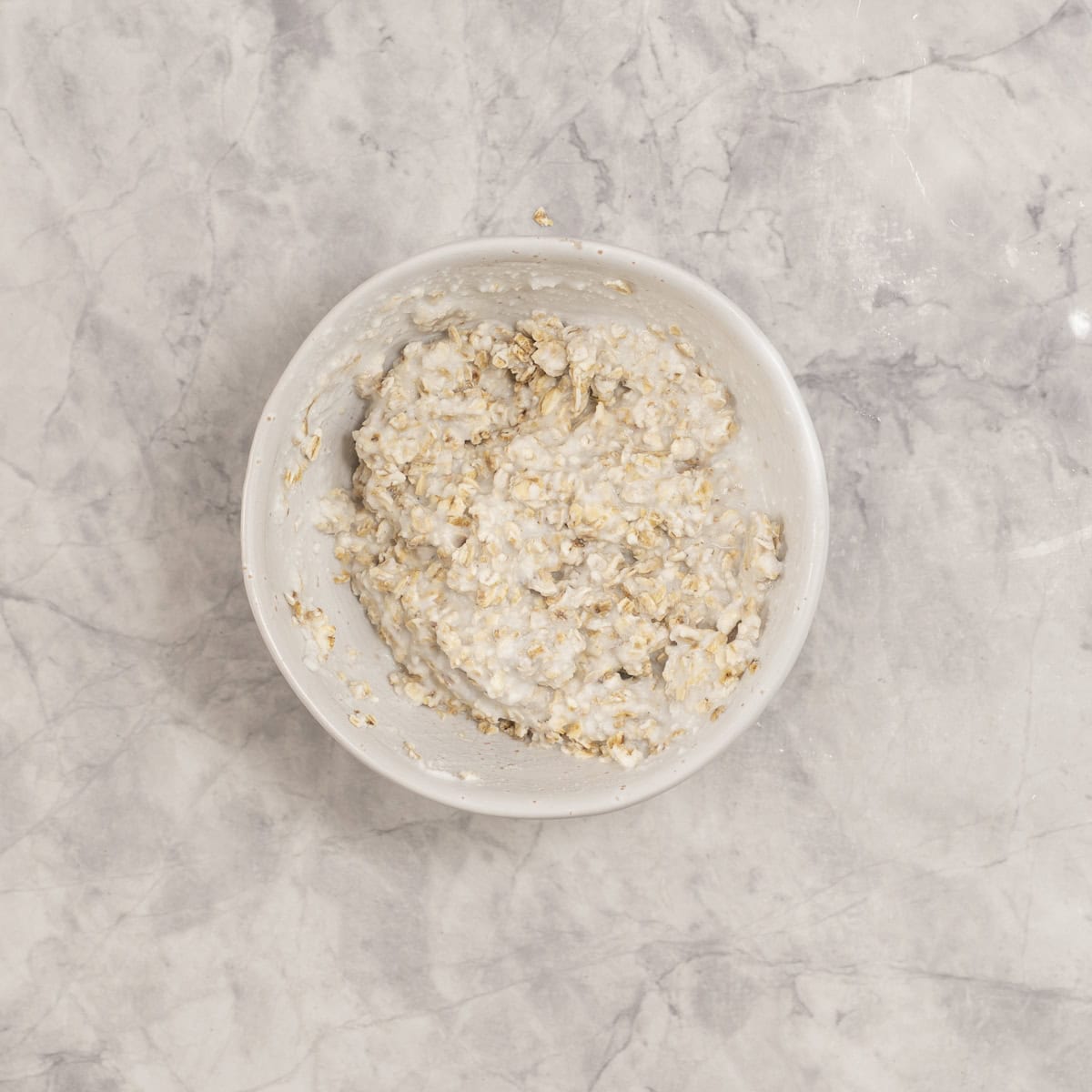 A bowl of oatmeal soaked in coconut milk on a marble counter.