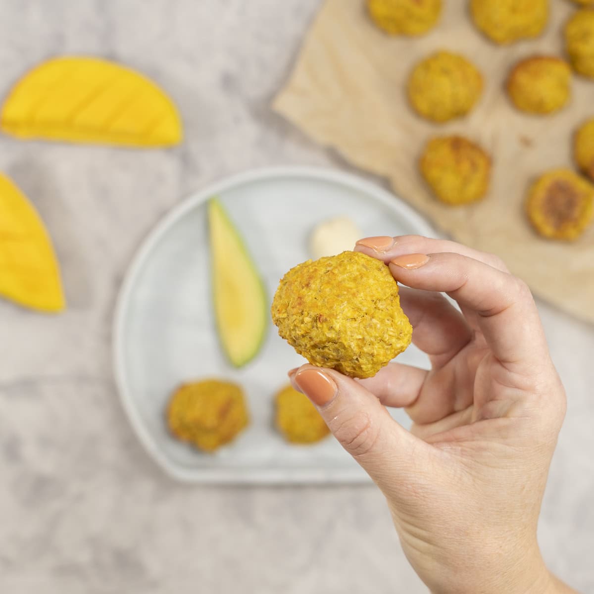 A person holding a piece soft chicken meatball with a mango n a counter.