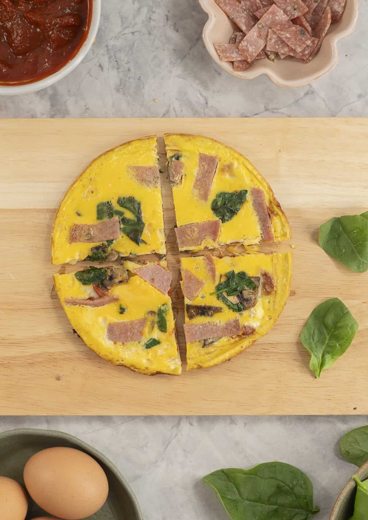 Wooden chopping board with pizza egg cut into four slices, toppings on bench top.