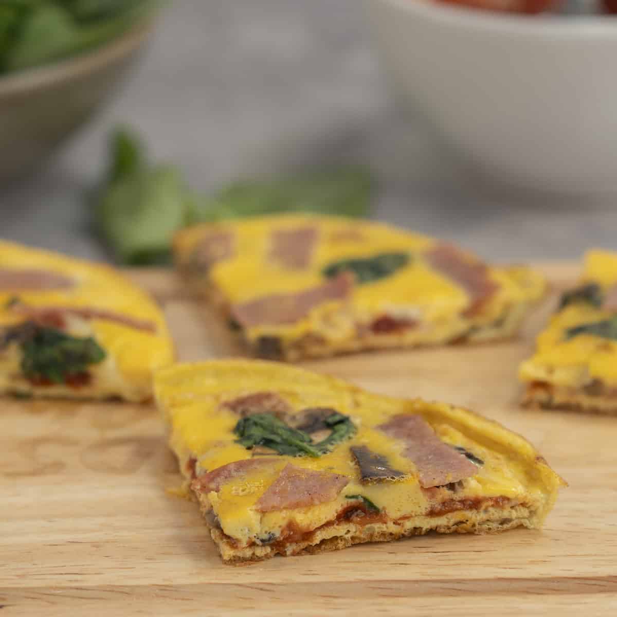Pizza eggs on wooden chopping board sliced into quarters showing the inside layers.