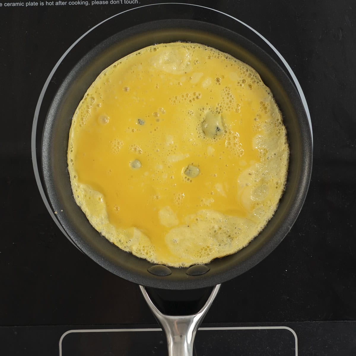 Egg in a skillet cooking in a thin layer on an electric stove top.