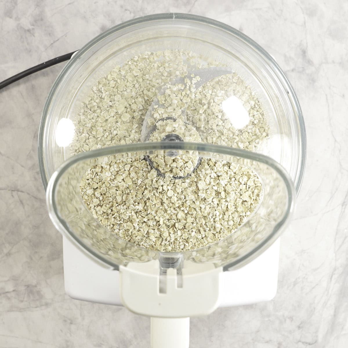 Food processor sitting on marble bench top with oats inside.