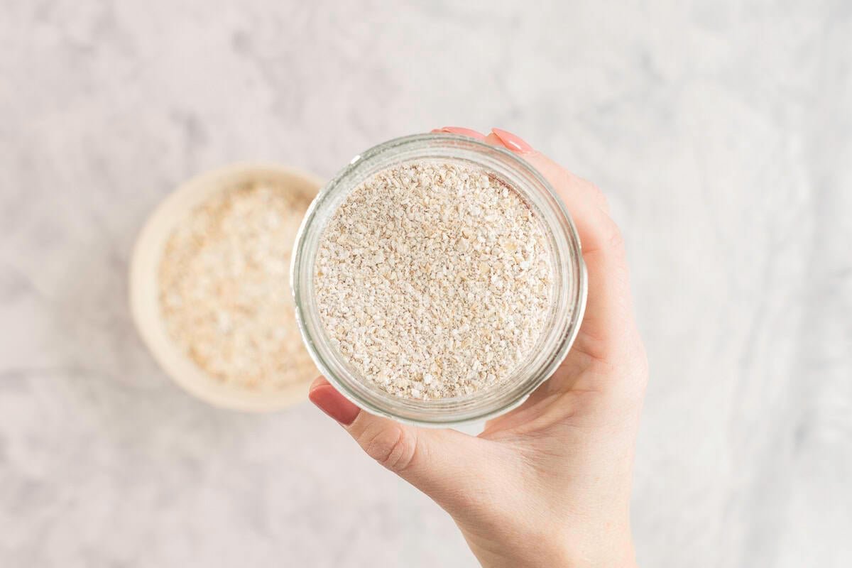 Womans hand holding a small jar of ground oats.