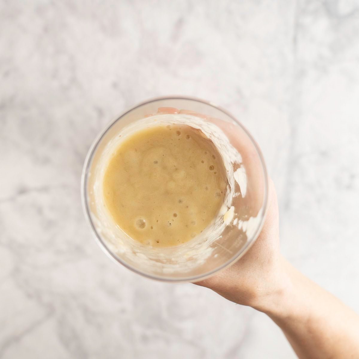 Hand holding a tall plastic cup with banana mixture inside.