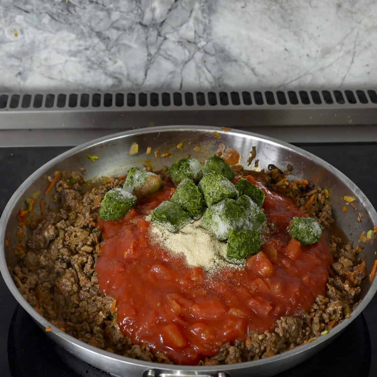 Tinned tomatoes, spinach and dried herbs added into pan on top of browned mince and vegetables.