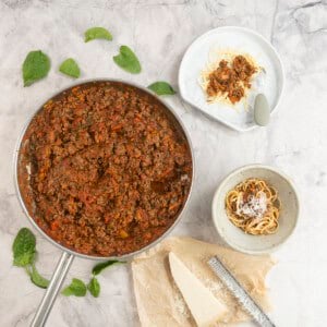 Sauce pan of bolognese on benchtop next to a dinner bowl and a baby plate with serving inside.