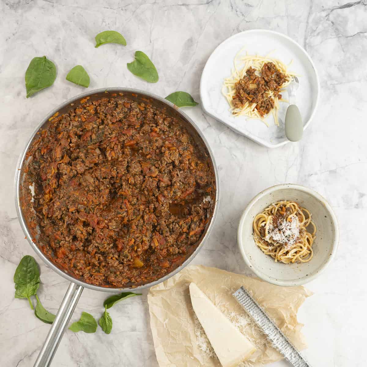 Sauce pan of bolognese on benchtop next to a dinner bowl and a baby plate with serving inside.
