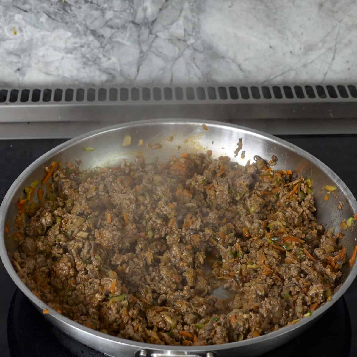 Mince and vegetables browned in a pan on stove top.