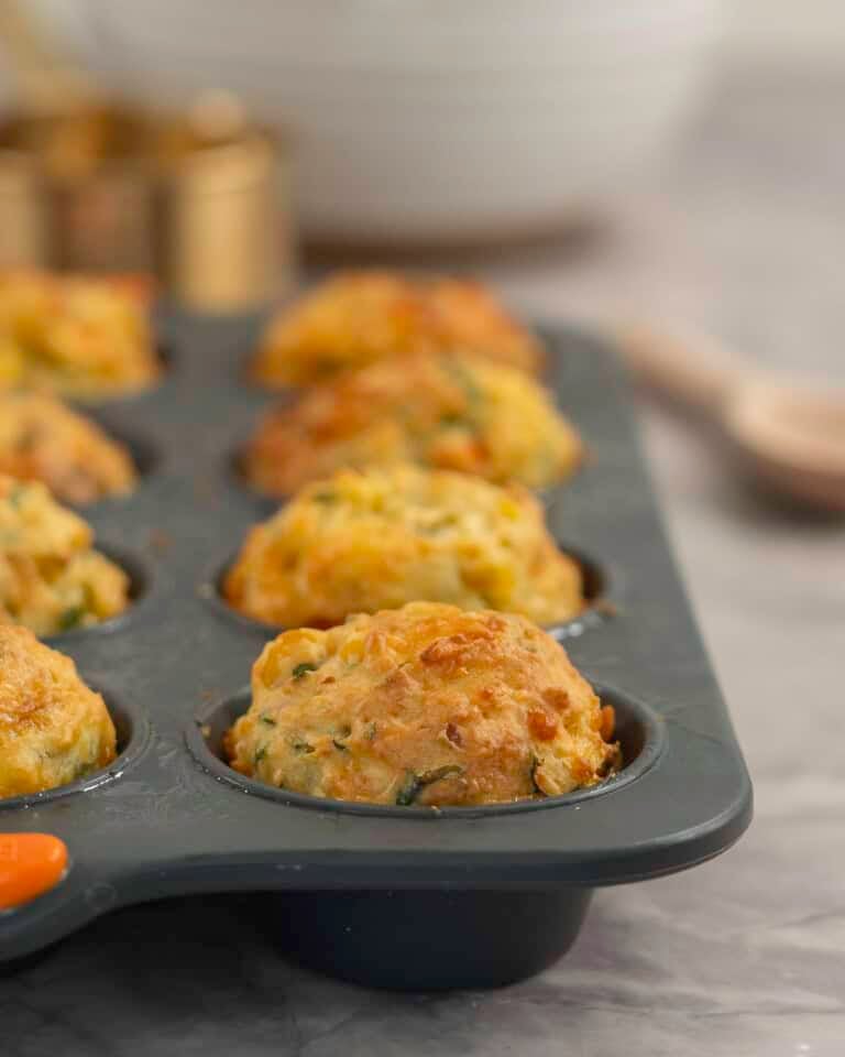 Cooked muffins packed with vegetables golden in colour inside a muffin tray on bench top.