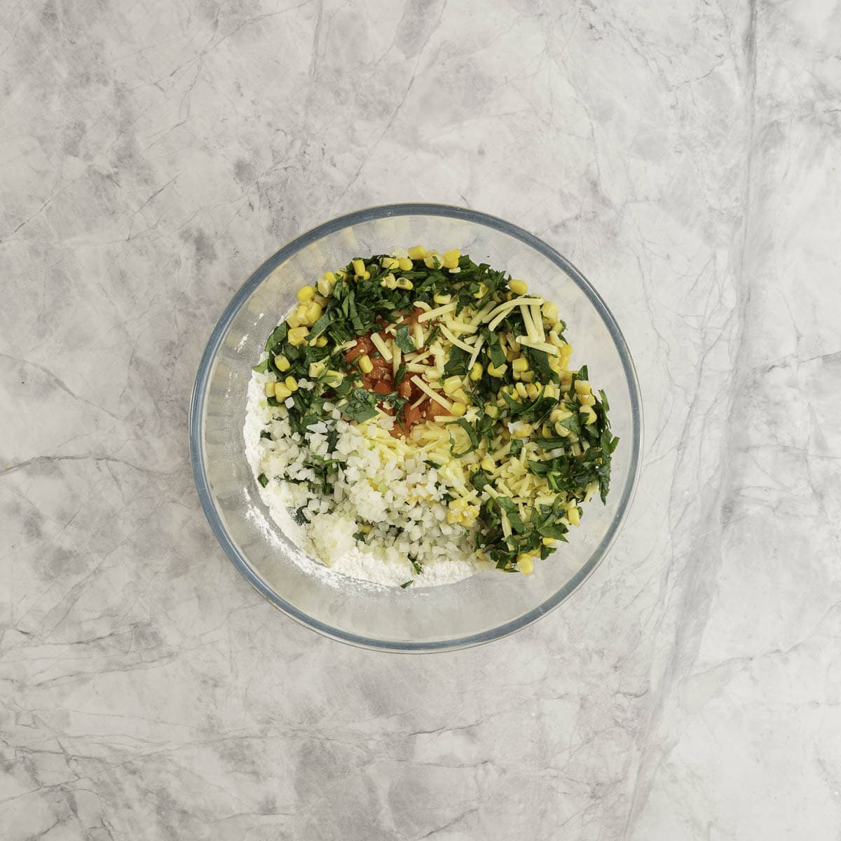 Vegetables and cheese added into glass bowl with flour inside.