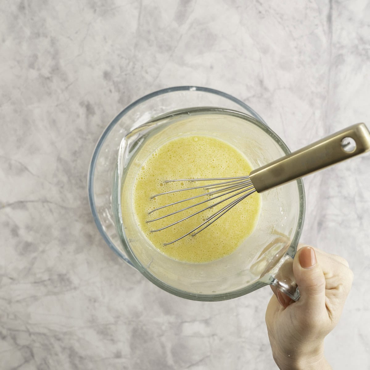 Hand holding a jug with wet ingredients and whisk inside.