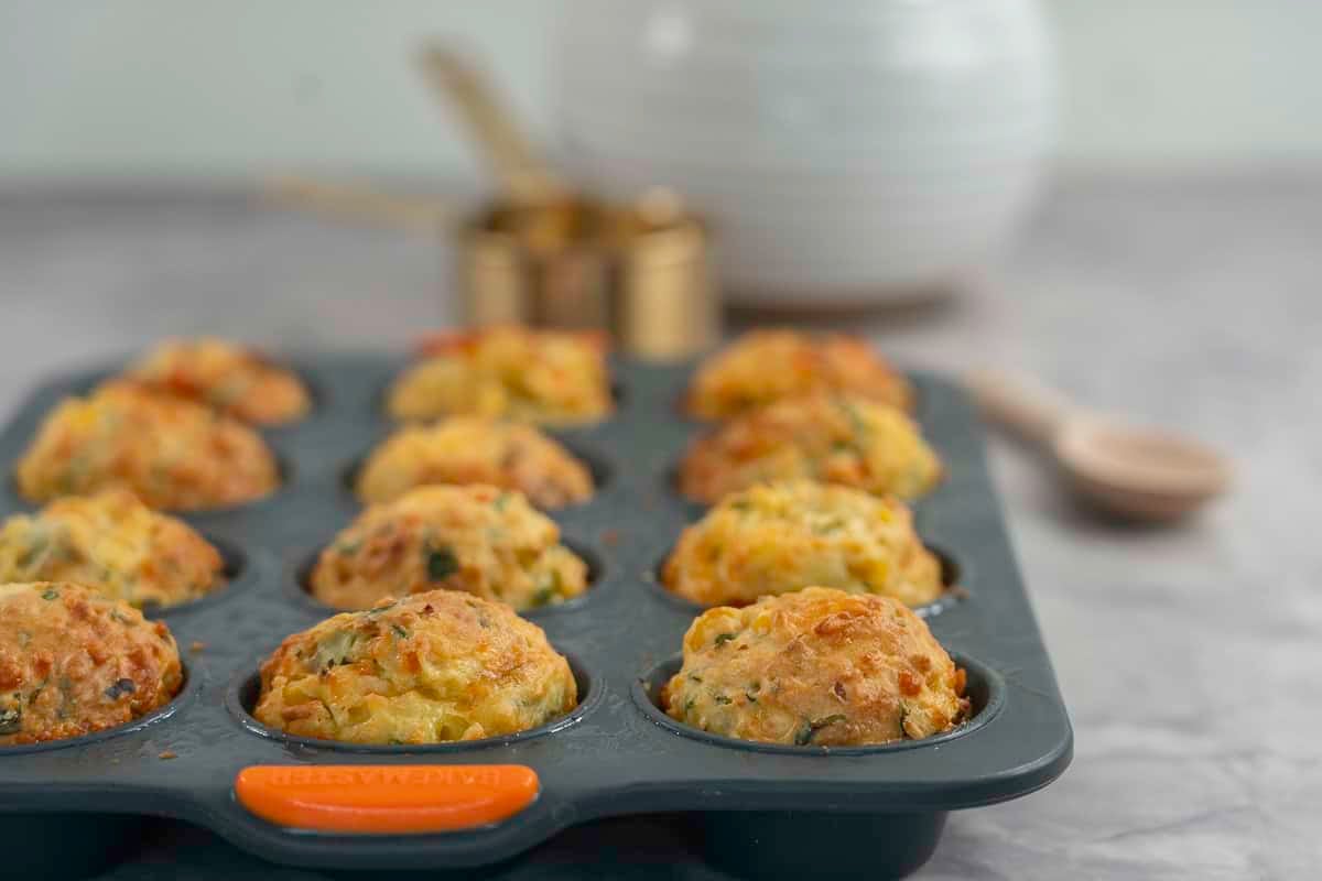 Cooked vegetable muffins golden in colour inside a muffin tray on bench top.
