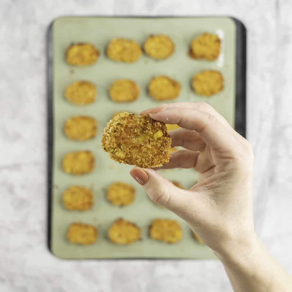Womans hand holding a crispy nugget above tray of nuggets below.