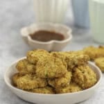 Dinner plate with a stack of crispy brown nuggets, sauce in small ramekin in background and colourful blue and green pastel cups.