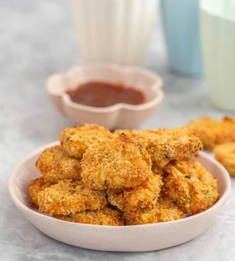 Dinner plate with a stack of crispy brown nuggets, sauce in small ramekin in background and colourful blue and green pastel cups.