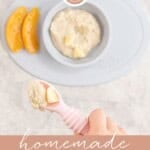 Toddler hand holding a silicone pink baby spoon with oatmeal and banana on its baby placemat and bowl with oats, and sliced canned peaches below next to a jar of ground oats on benchtop. Text overlay; homemade baby oatmeal.