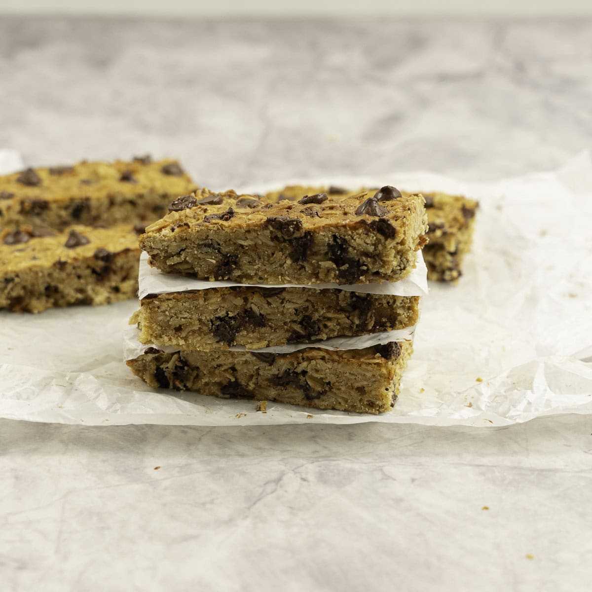 Three slices of granola bars stacked on one another with baking paper in-between.